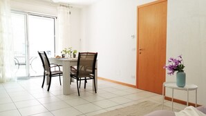 A dining area with a table and chairs, a small side table with a vase, and a sliding glass door leading to a balcony.