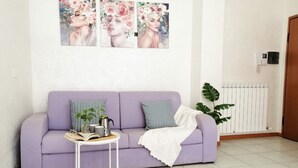 A living room with a purple sofa, a small white table with a book and a plant, and a radiator.