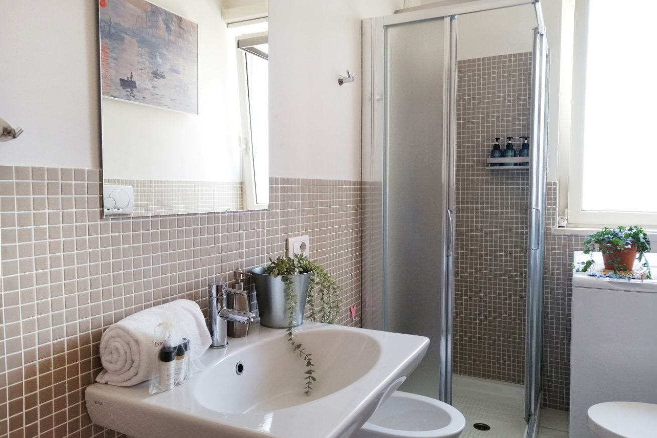 A bathroom with a white sink, a mirror, a towel, a plant, and a shower area.