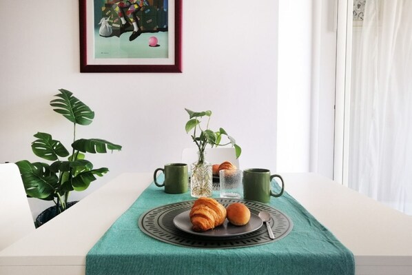 Una mesa de comedor con mantel verde, dos croissants, un vaso de agua y dos tazas verdes.