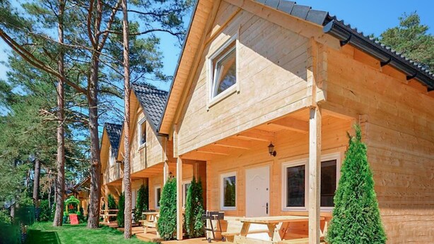 A wooden cabin with a porch, a dining area, and a small play structure. - Cozy home in Pobierowo with WiFi (Pobierowo)
