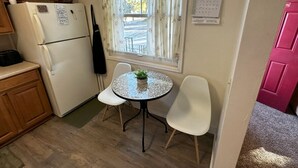A compact kitchen with a refrigerator, a small dining table with chairs, a window with curtains, and a calendar on the wall. - Pet Friendly 2BR Home w/ fenced backyard (Billings)