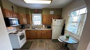 A compact kitchen with wooden cabinets, a white stove, a refrigerator, and a small dining table with a plant. - Pet Friendly 2BR Home w/ fenced backyard (Billings)