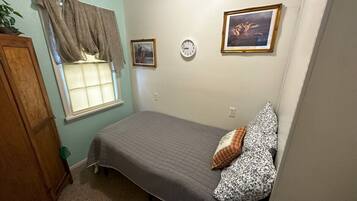 Un dormitorio con cama, ventana con cortinas, un reloj de pared y cuadros enmarcados.
