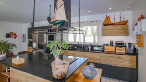 Una cocina moderna con una isla central, electrodomésticos de acero inoxidable y un amplio ventanal con cortinas.