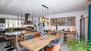 Una cocina moderna con una isla central, iluminación colgante y un comedor con mesa y sillas de madera.