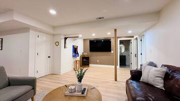 A modern living room with a sofa, a coffee table with a plant, and a TV mounted on the wall.