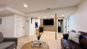 A modern living room with a sofa, a coffee table with a plant, and a TV mounted on the wall.