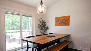 A dining area with a wooden table, benches, and chairs. There is a large window with a view of greenery outside.