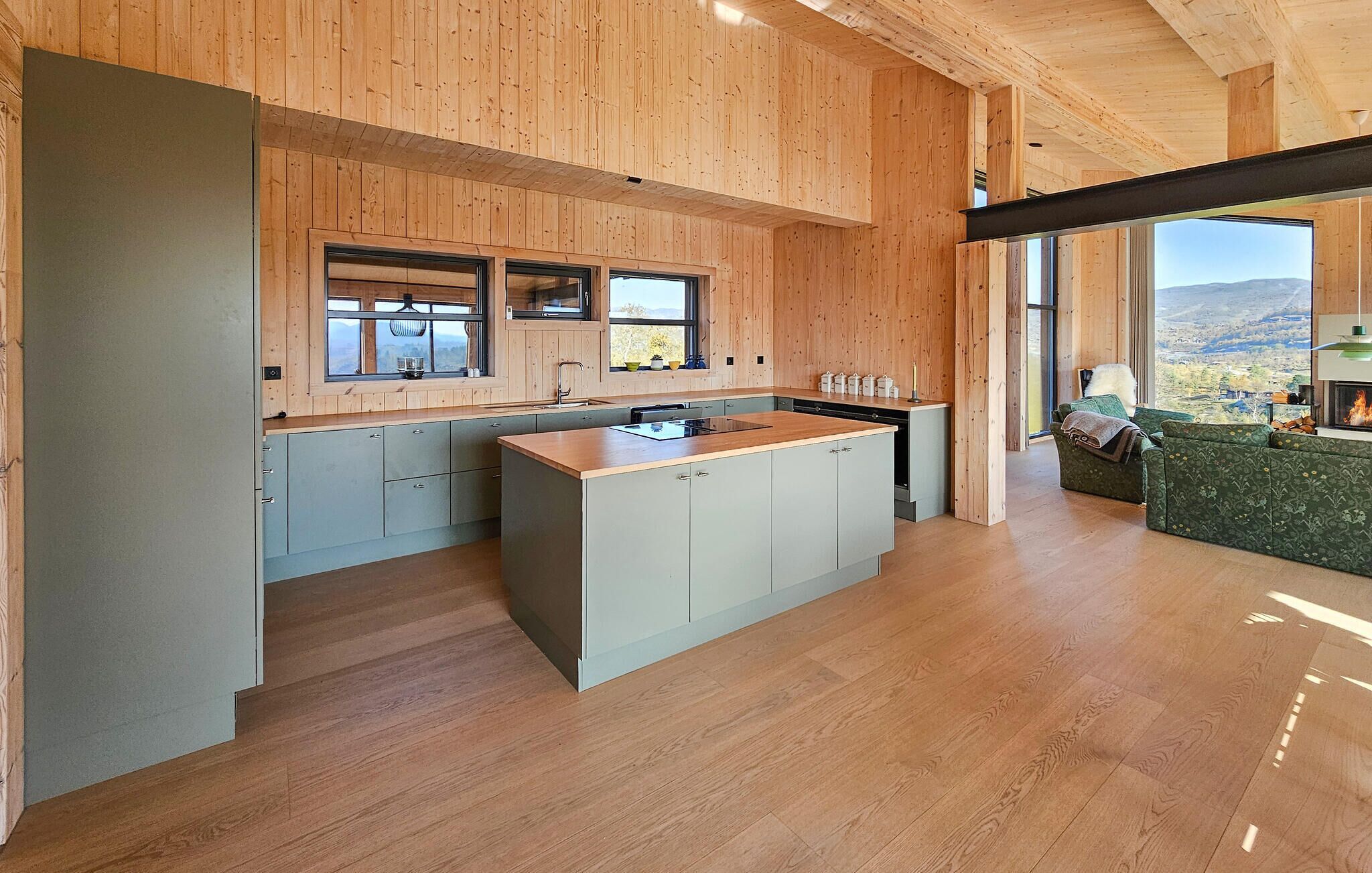 Une cuisine moderne avec un lambris en bois, un îlot central et de grandes fenêtres donnant sur l’extérieur.