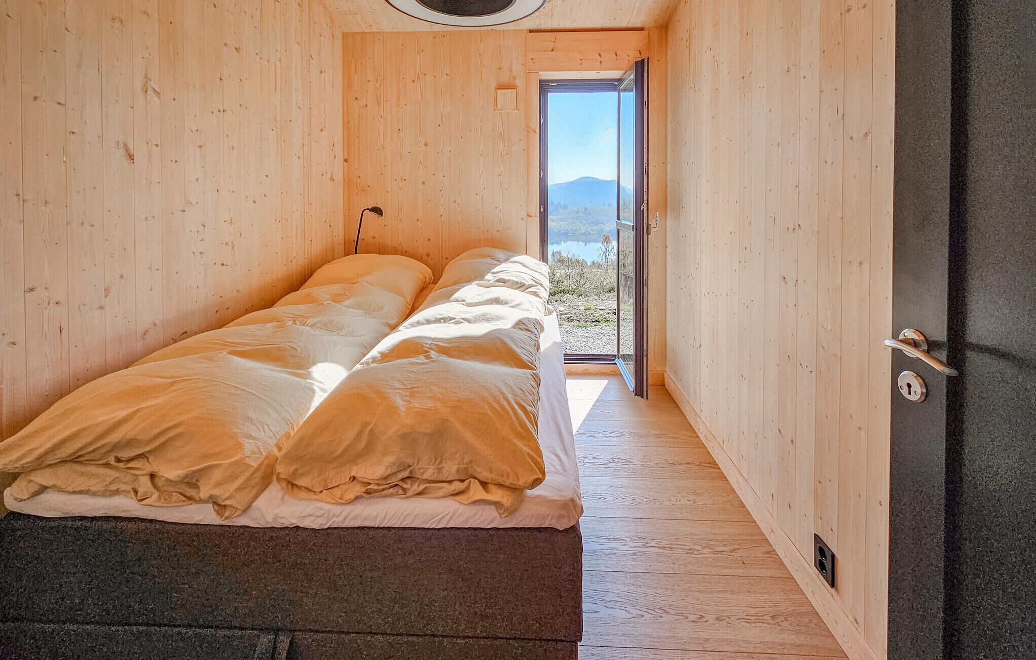 Une pièce en bois avec un lit et une porte donnant sur un espace extérieur d’où l’on peut admirer la vue sur les montagnes.