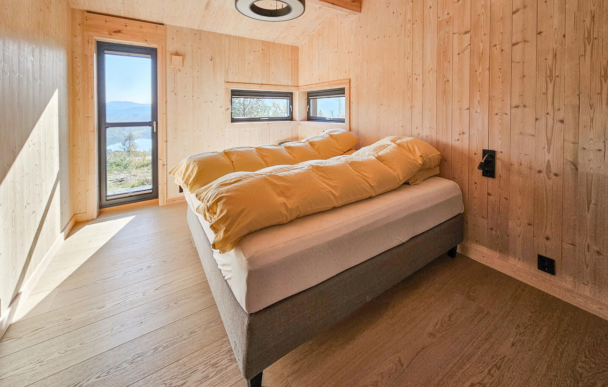 Un dormitorio con cama, paredes de madera y ventanas amplias.