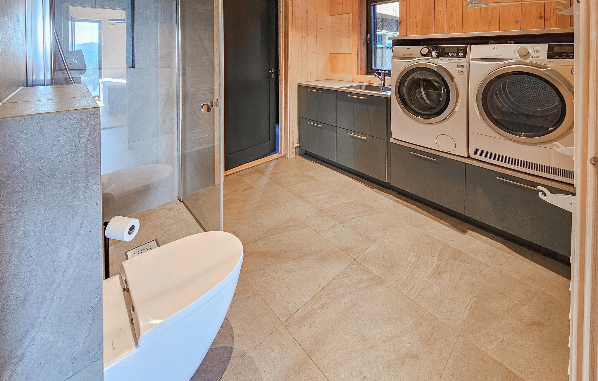 A modern bathroom with a toilet, a glass shower enclosure, and a washing machine.