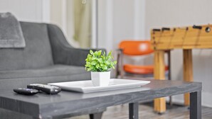 A living room with a grey sofa, a small white table with a potted plant, and a few remote controls on the table.