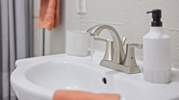 A bathroom sink with a modern faucet, a soap dispenser, and a glass of water.