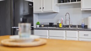 A kitchen with white cabinets, a black refrigerator, a sink with a modern faucet, and a countertop with a plant, a basket, and some toiletries. - 3 BR Cozy Home Near Indy Downtown , Foosball Table (Indianapolis)