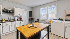 A compact kitchen with white cabinets, a wooden table, a coffee machine, and a washing machine. - 3 BR Cozy Home Near Indy Downtown , Foosball Table (Indianapolis)