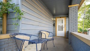 A covered patio with two metal chairs and a table, a door, and a brick wall. - 3 BR Cozy Home Near Indy Downtown , Foosball Table (Indianapolis)