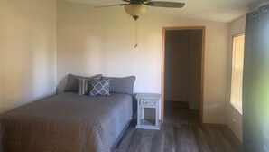Une chambre à coucher comprenant un lit, une table de chevet, un ventilateur de plafond et une fenêtre avec des stores.