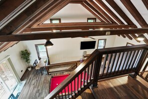 A wooden staircase leading to a red pool table in a room with a TV and a potted plant.