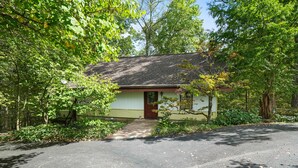 A single-story house with a front porch, surrounded by trees and a driveway.