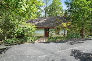 A single-story house with a front porch, surrounded by trees and a driveway.