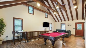 Um quarto espaçoso com mesa de bilhar, piso de madeira e teto alto com vigas aparentes.