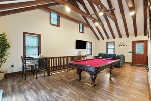 Ein geräumiges Zimmer mit Poolbillard, Holzboden und hohen Decken mit freiliegenden Balken.