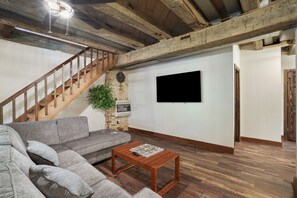 A living room with a wooden staircase, grey sofa, and a flat-screen TV mounted on the wall.