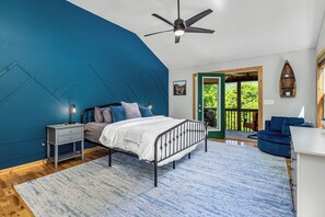 Une chambre à coucher comprenant un lit, une table de chevet, un bureau et donnant sur l’extérieur.