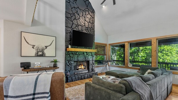 A modern living room with a stone fireplace, a large flat-screen TV, and a cozy seating area. - Moose Shack - Mountain Views · Spa King Suite · Game Room · 3 Patios (Blairsville)