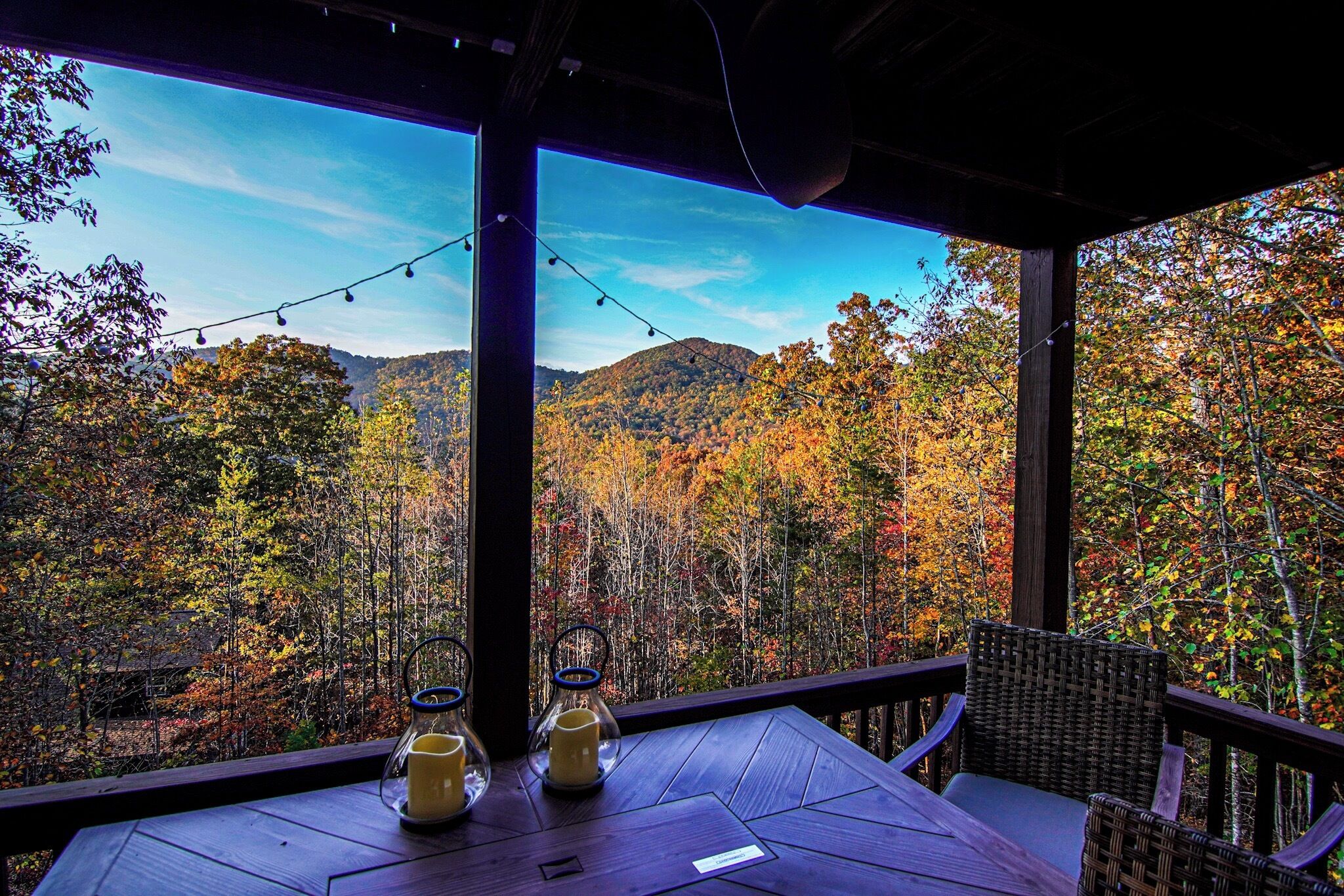 A wooden deck with a table and chairs, overlooking a forested mountain range.