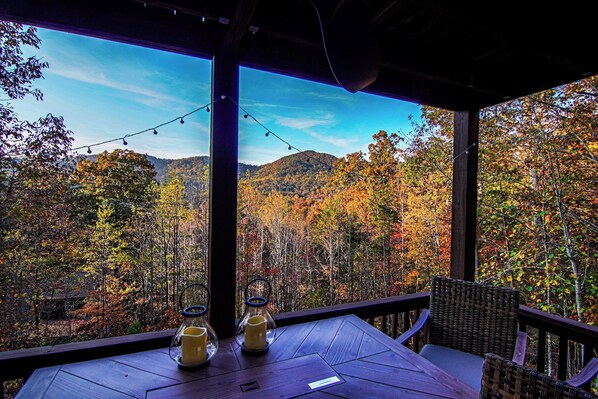 A wooden deck with a table and chairs, overlooking a forested mountain range.