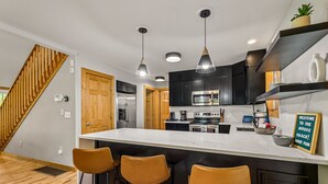 A modern kitchen with a large island, black cabinets, stainless steel appliances, and a wooden staircase. - Moose Shack - Mountain Views · Spa King Suite · Game Room · 3 Patios (Blairsville)