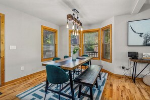 A dining area with a wooden table, teal chairs, a bench, and a hanging light fixture. - Moose Shack - Mountain Views · Spa King Suite · Game Room · 3 Patios (Blairsville)