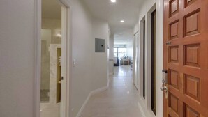 Un couloir avec une porte en bois, un interrupteur et un spot encastré au plafond.