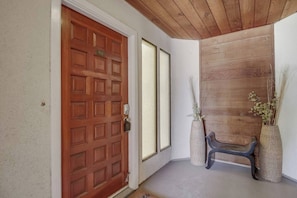 Una puerta de madera con cerradura electrónica, un banco y dos altos jarrones con plantas.