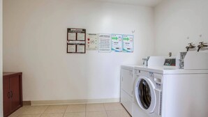 Une buanderie équipée d’un lave-linge, d’un sèche-linge et de divers affiches informatives accrochées au mur.