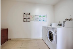 A laundry room with a washing machine, a dryer, and various informational posters on the wall.