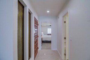 Un couloir étroit, avec un lit visible au fond, une porte sur la droite et une porte à motifs sur la gauche.