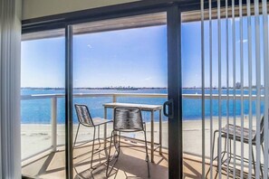 A balcony with two metal chairs and a small table, overlooking a body of water with a distant shoreline.