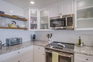 Une cuisine moderne avec des meubles blancs, un four à micro-ondes encastré, un grille-pain et une cuisinière.