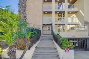 A multi-story building with a staircase leading to the entrance, surrounded by greenery.