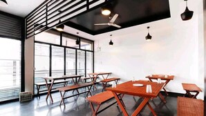 A modern dining area with wooden tables and benches, large windows, and ceiling fans. - HOTEL PLAZA AVENUE  (Mangaluru)