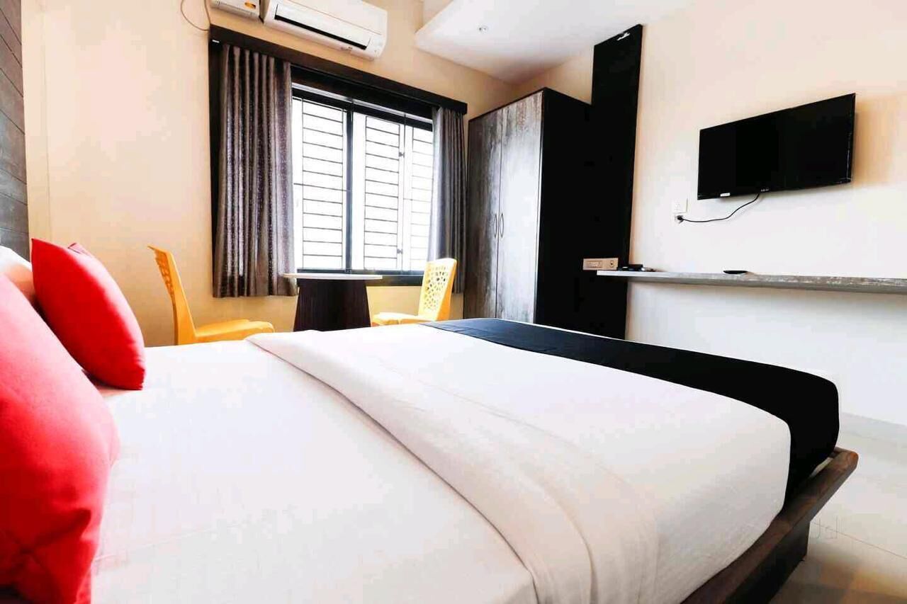 A hotel room with a bed, a TV mounted on the wall, a window with curtains, and a wardrobe.