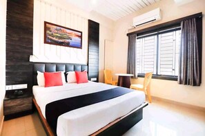 Quarto de hotel com uma cama grande, um quadro na parede, uma janela com cortinas e uma pequena mesa com uma cadeira.