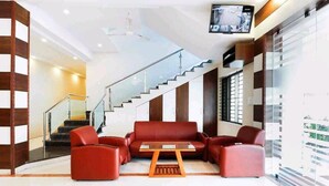 A modern lobby with a staircase, red leather seating, and a flat-screen TV. - HOTEL PLAZA AVENUE  (Mangaluru)