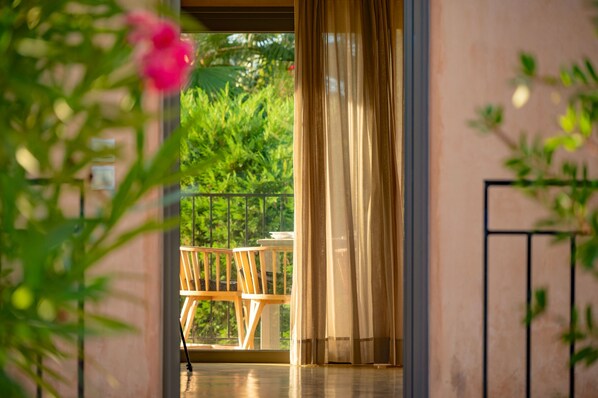 An outdoor balcony with a wooden chair and table, a glass door, and greenery in the background. - Relax at Villa Rhea, just a short walk from the beautiful Ai Helis Beach (Svoronata)