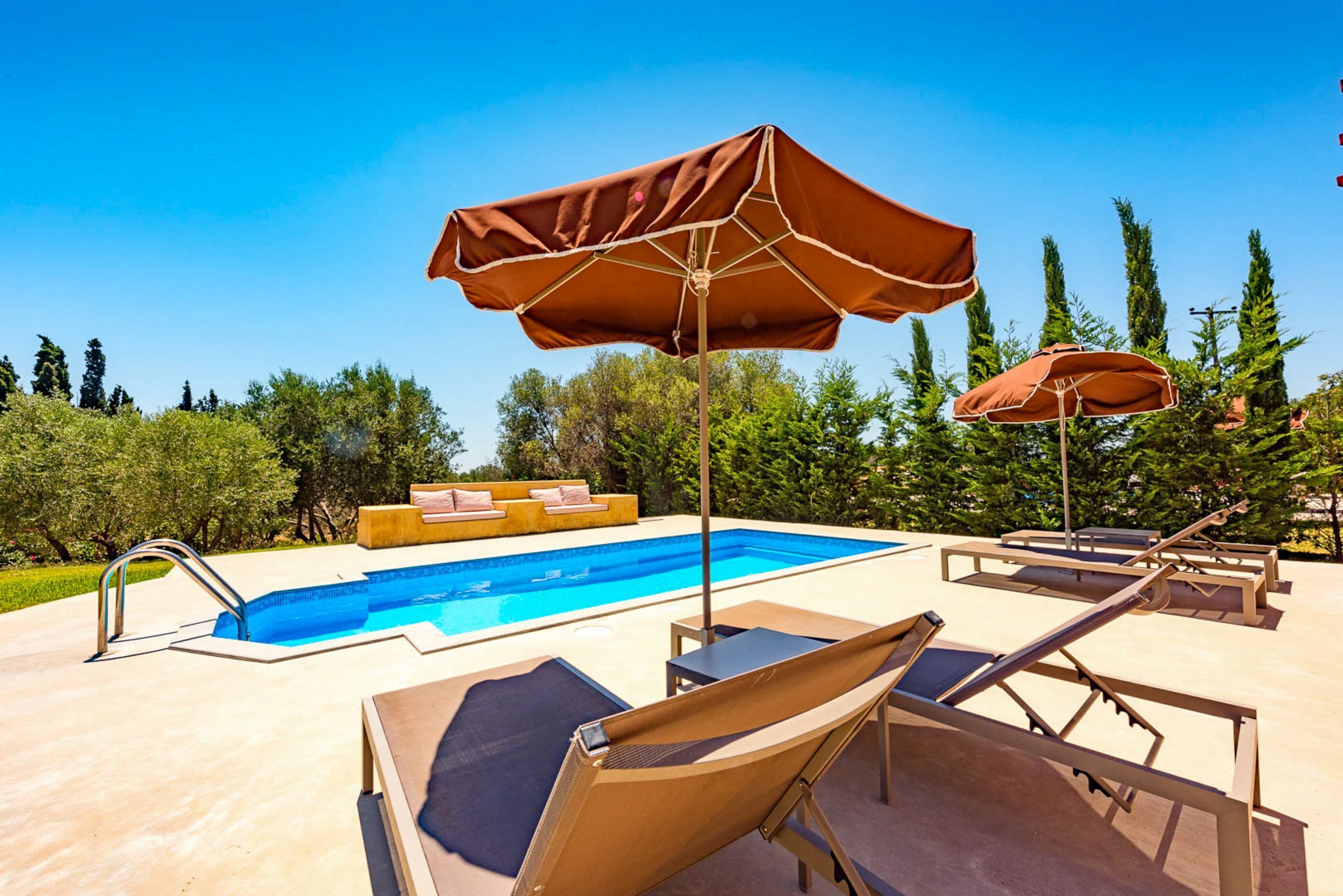 Un espace piscine équipé de chaises longues, de parasols et d’un coin salon.