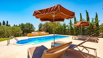 Un espace piscine équipé de chaises longues, de parasols et d’un coin salon.